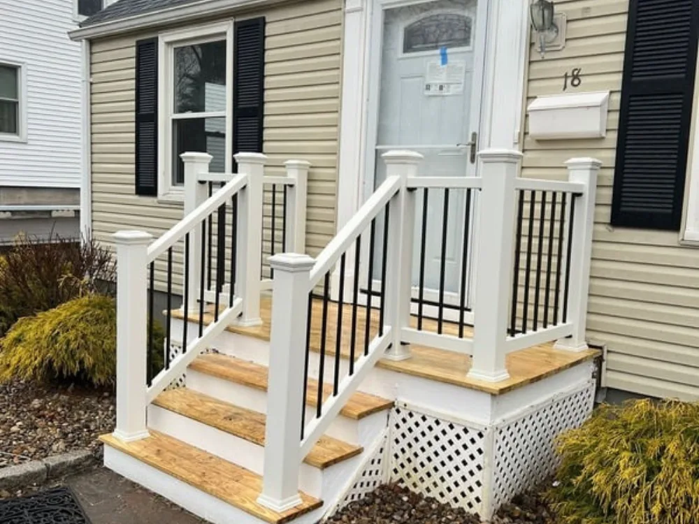 Front porch renovation with new white posts, black railings, and wooden steps.