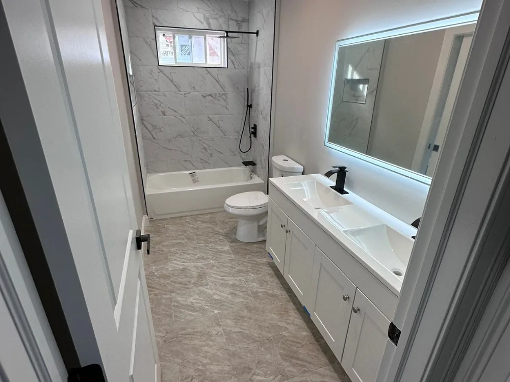 View from the entrance showing the completed full bathroom remodel with marble-look tiles, a white tub, and black shower fixtures.