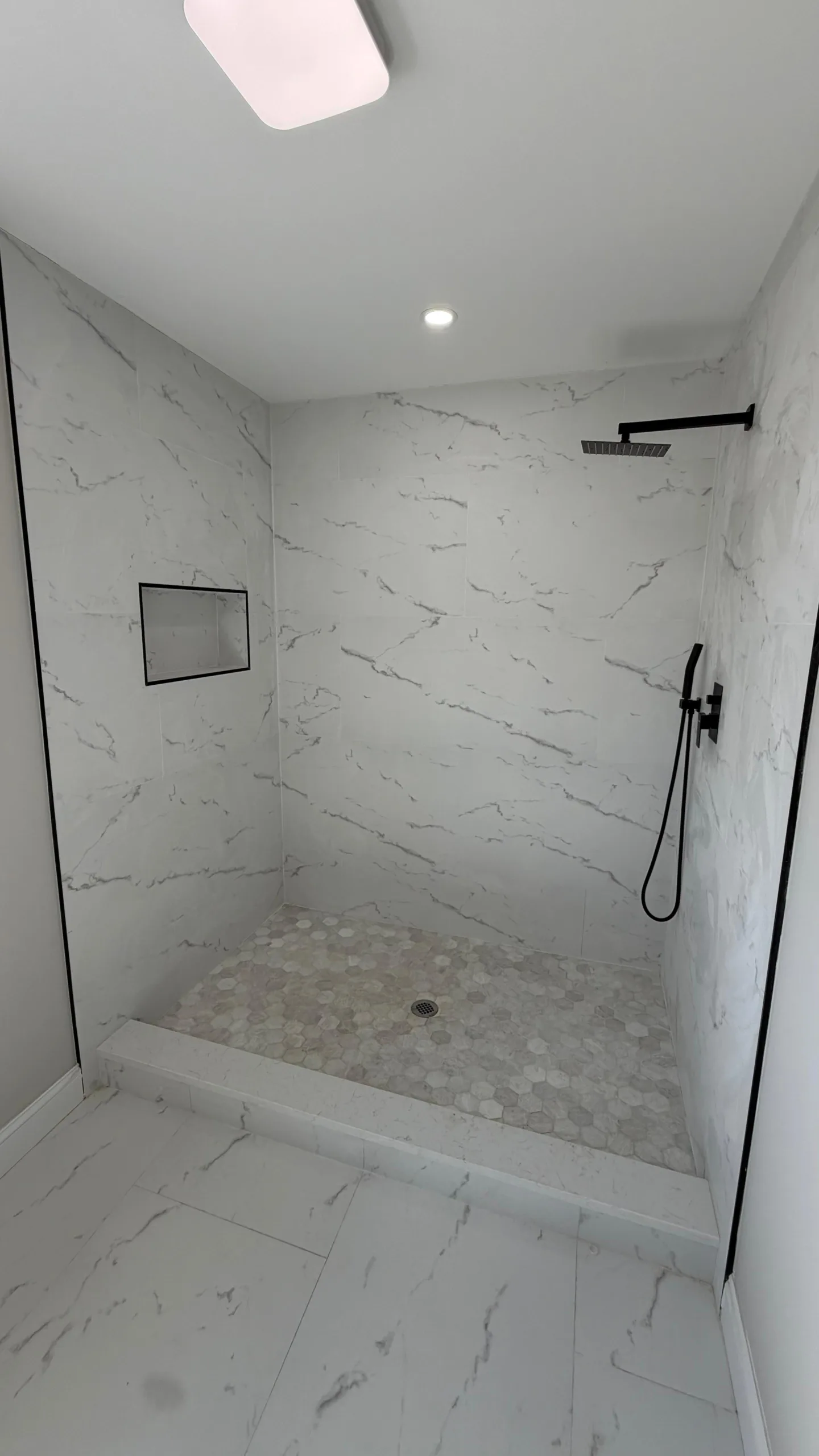 Modern marble bathroom remodel featuring a walk-in shower with matte black rain shower head and matching handheld sprayer.