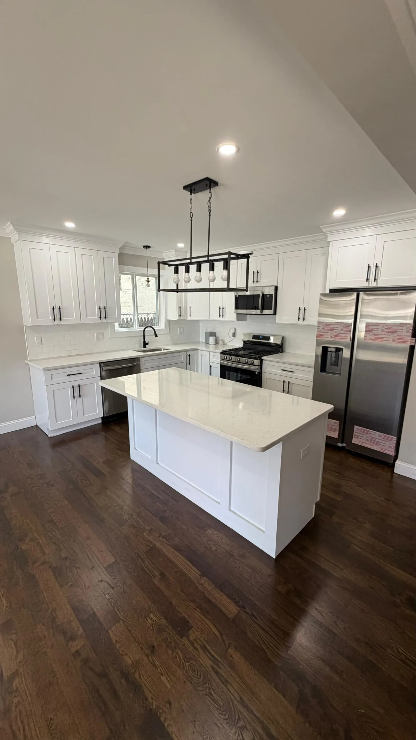Modern white kitchen renovation featuring shaker cabinets, a large center island, and dark hardwood flooring.