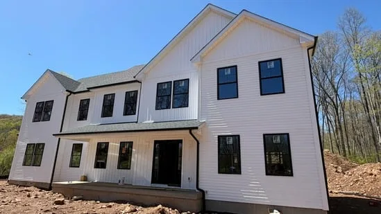 Angled front perspective highlighting modern farmhouse exterior siding and completed roofline drainage.
